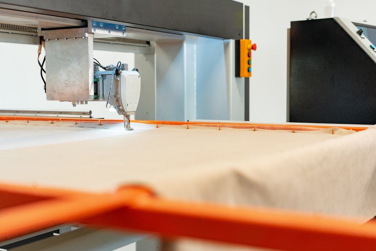 Maszyna nad rozłożoną tkaniną techniczną w jasnej hali produkcyjnej
